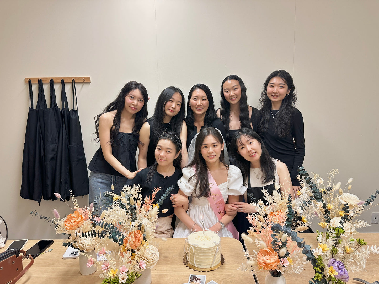 Group of women posing together with a cake and floral arrangements on a table.