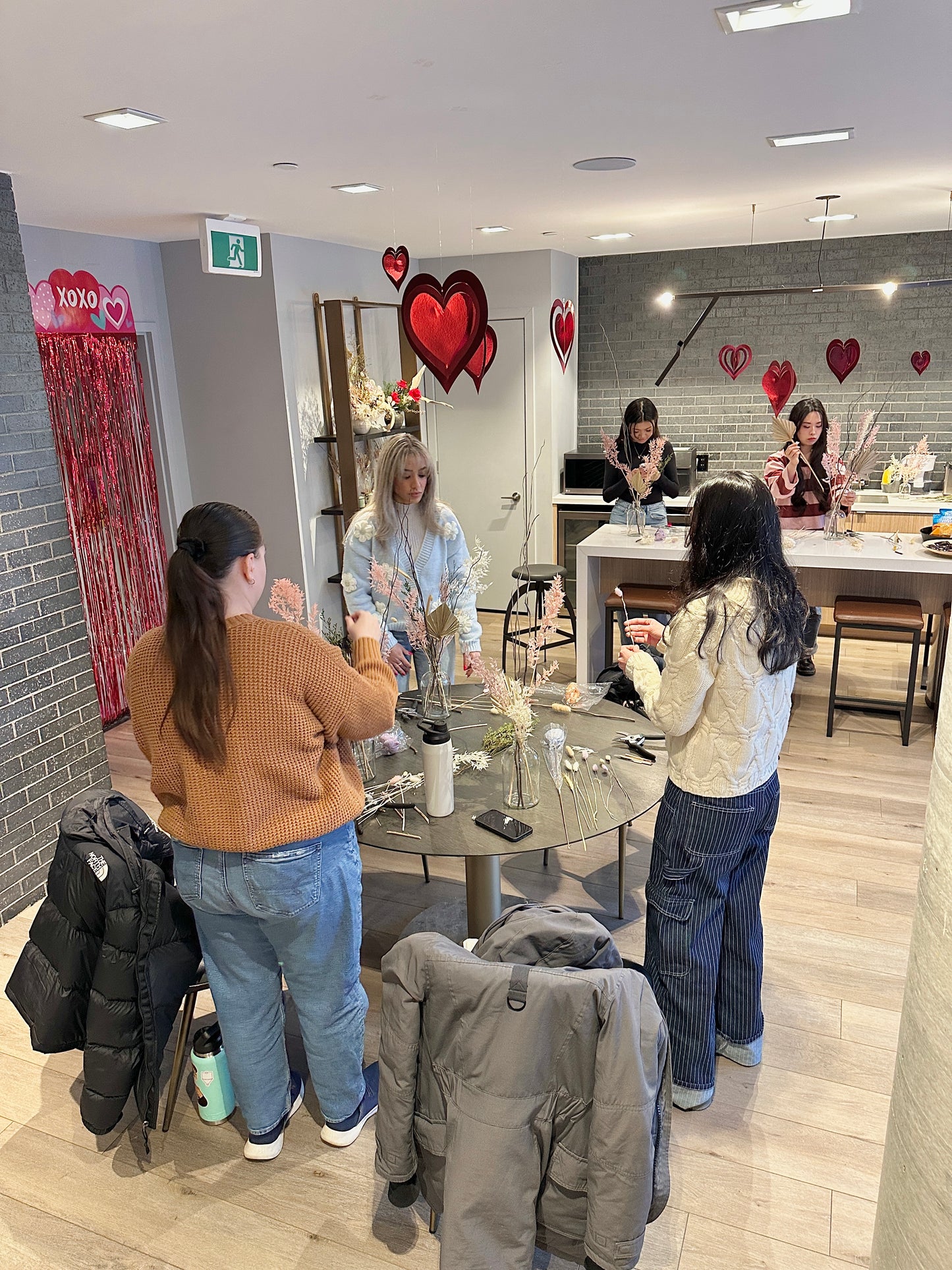 Group of people making dried flower arrangements in a modern interior setting with decorative hearts on the wall.
