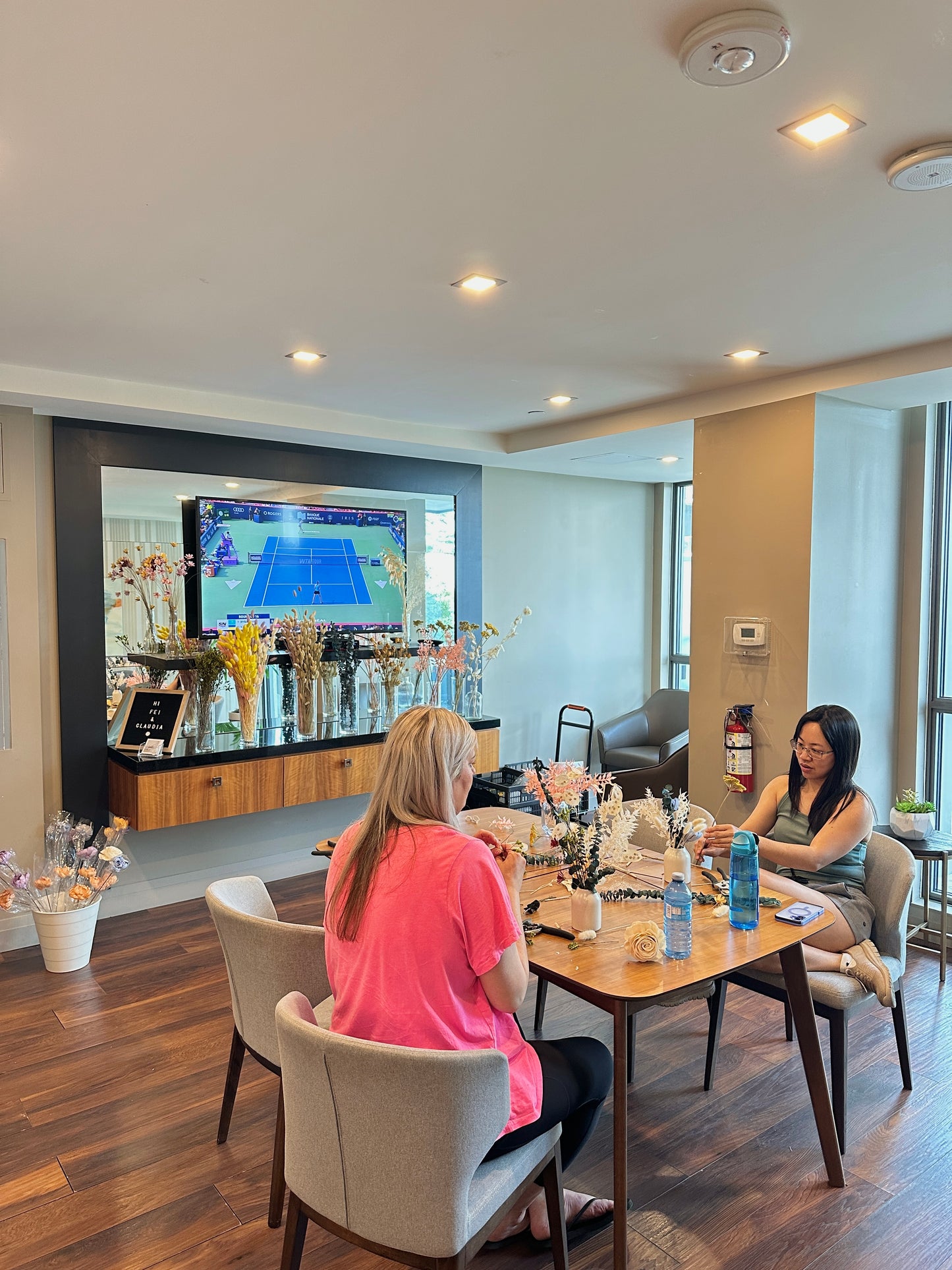 Two women sitting at a table in a modern living room creating dried flower arrangements.