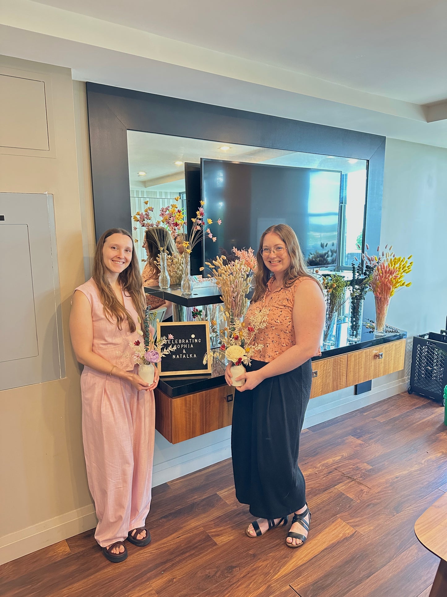 Two women holding flower arrangements in a modern interior setting