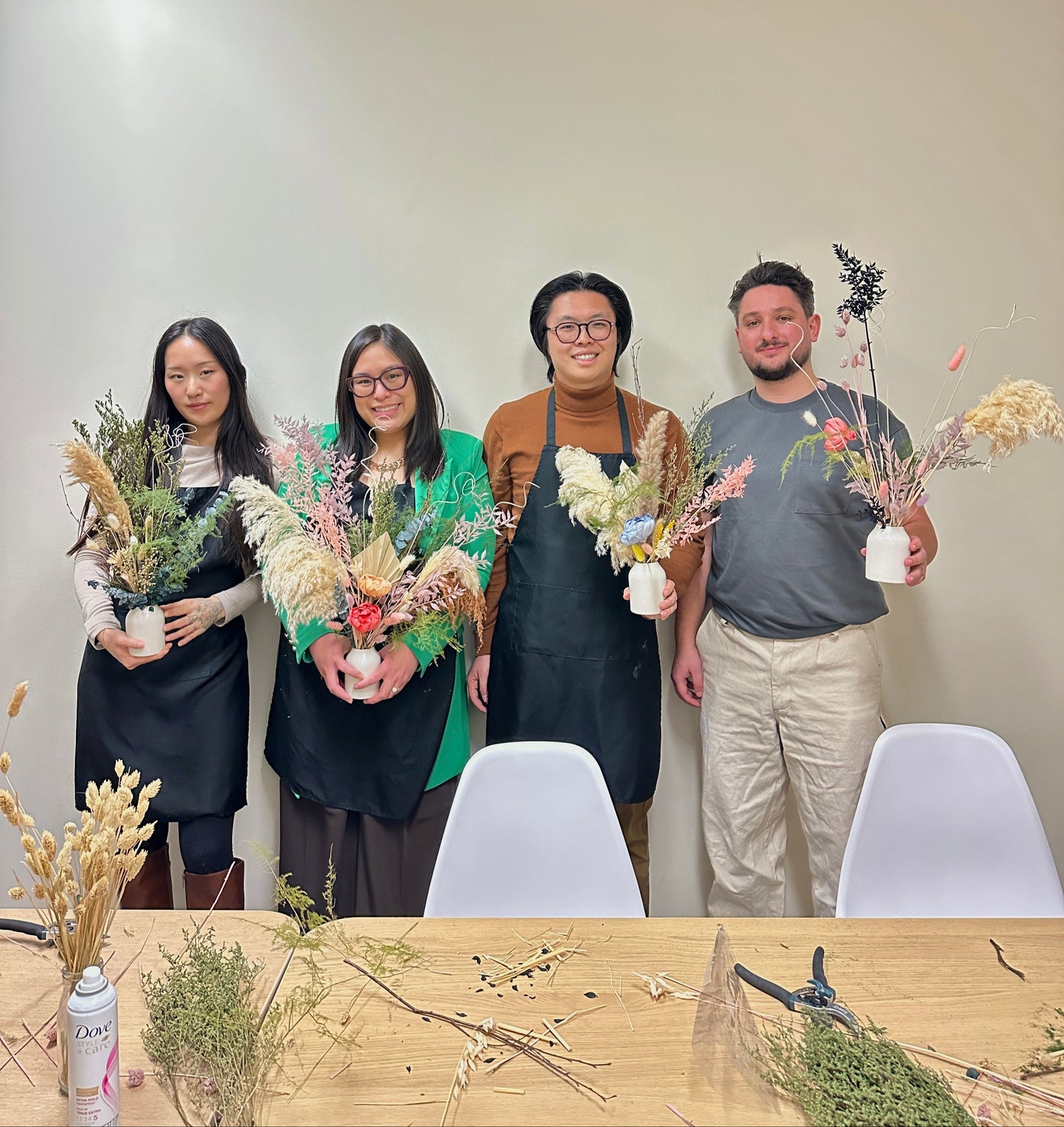Four people standing behind a table with floral arrangements in an indoor setting.