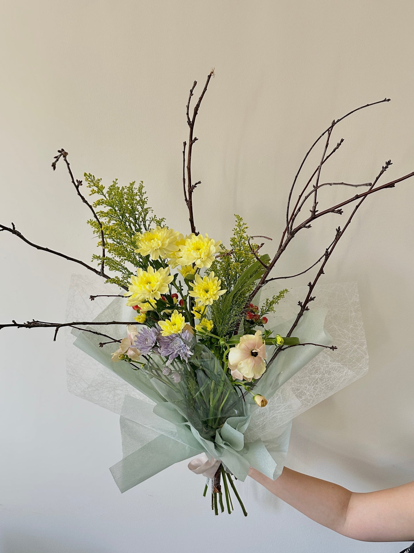 Bouquet of flowers with yellow and green colours held against a plain background