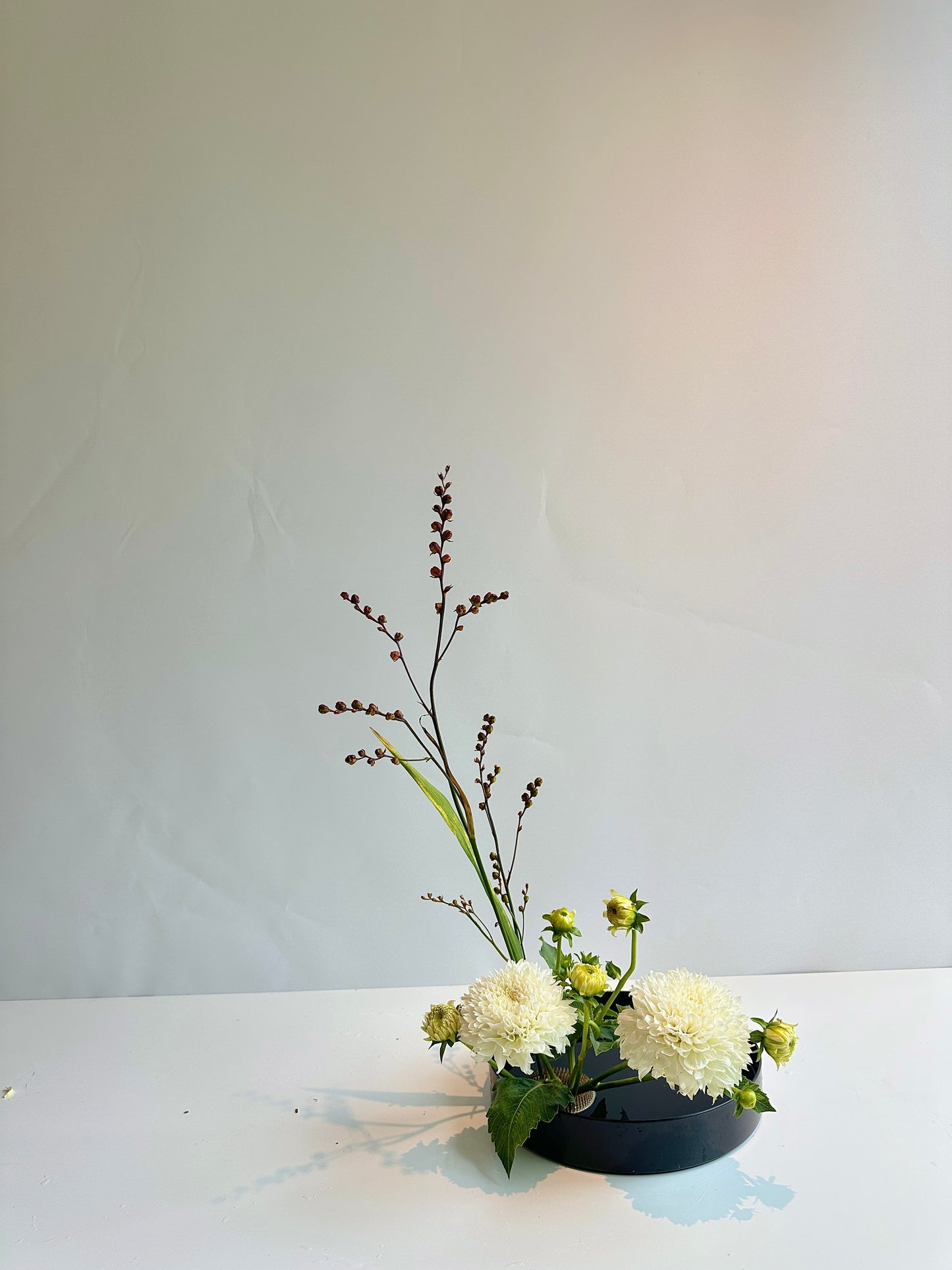 Floral arrangement in a black low bowl on a white surface with a light gray background