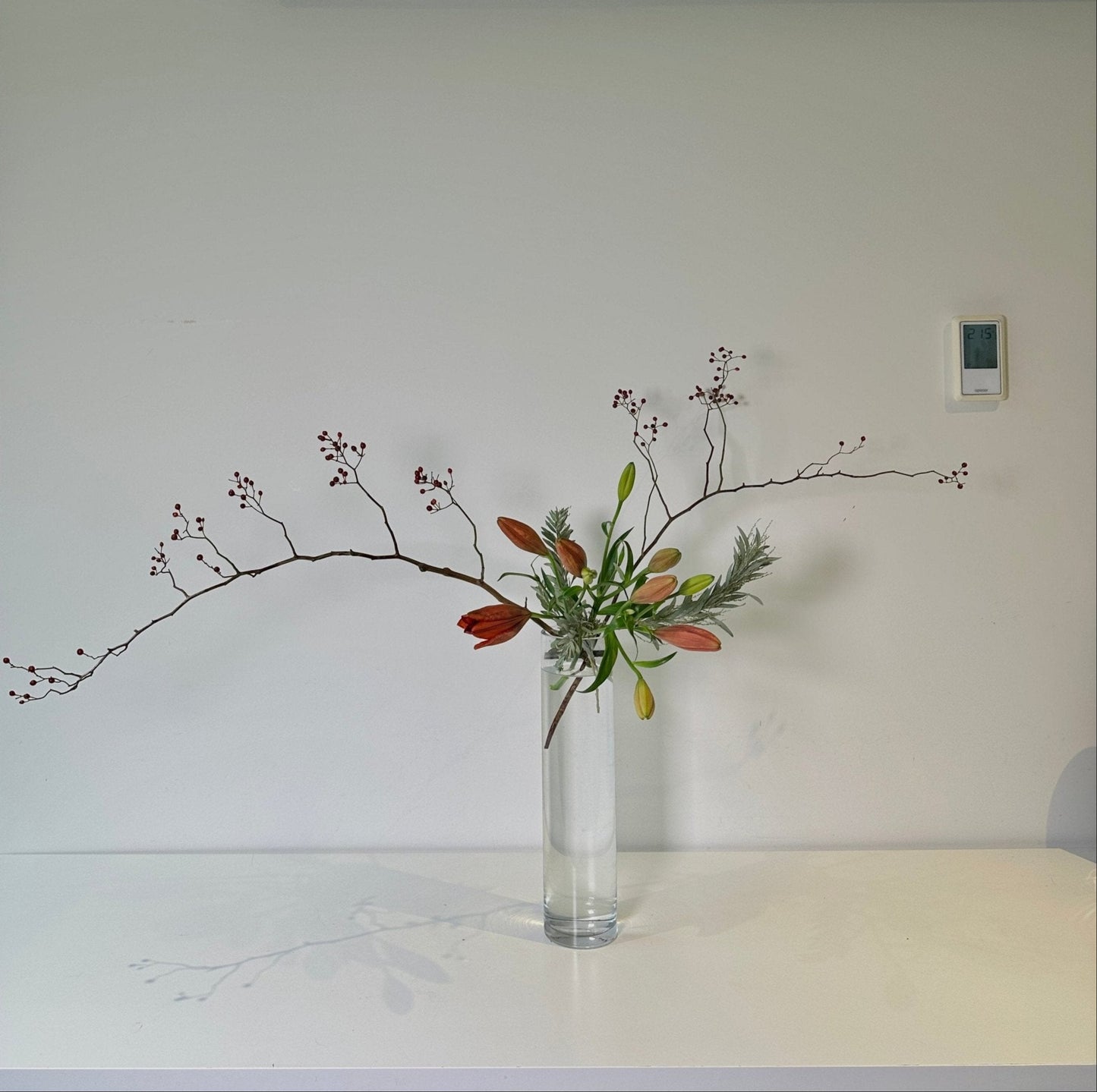Clear vase with flowers on a white surface against a plain wall
