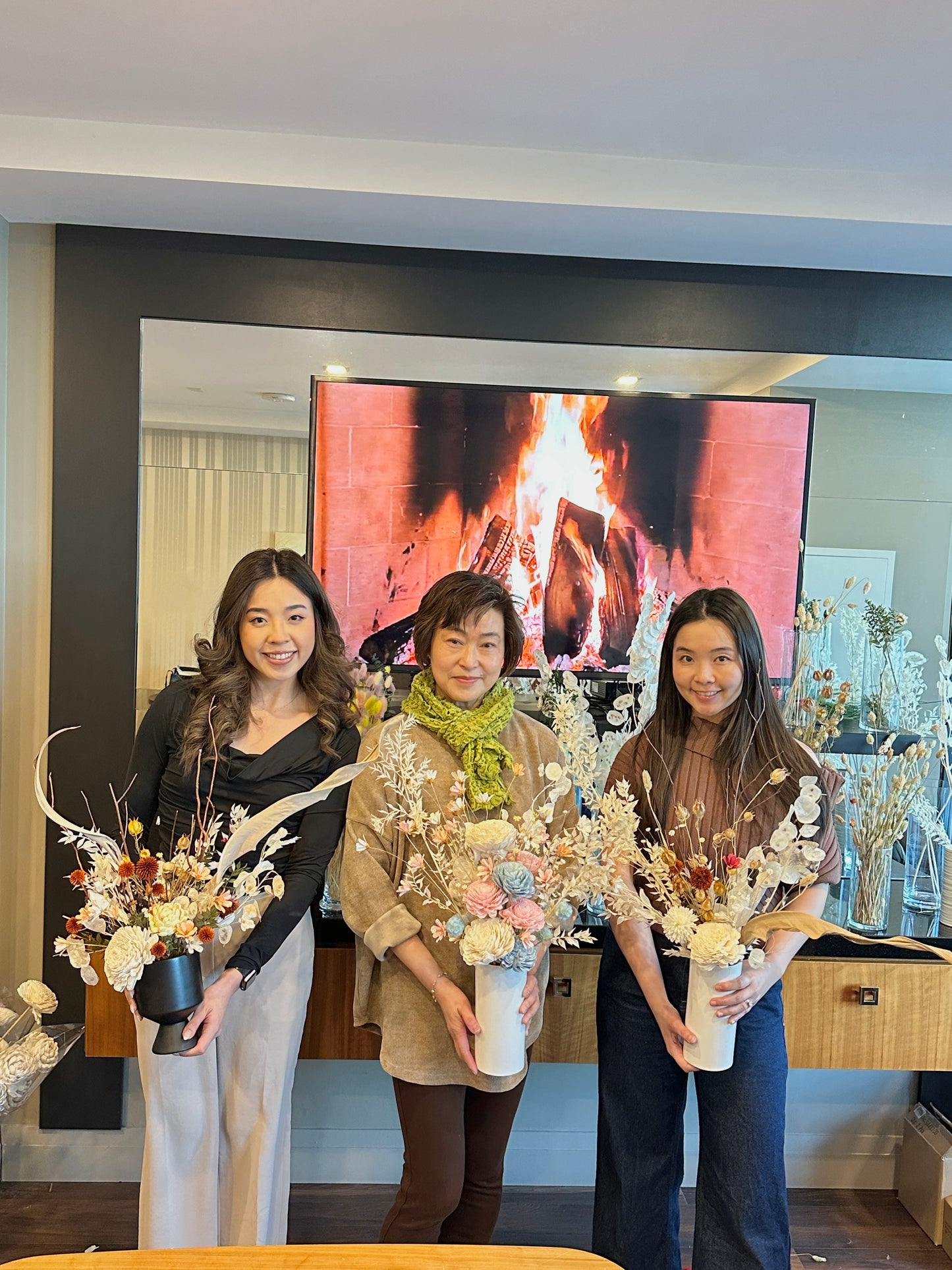 Three women holding floral arrangements in a room with a television screen in the background.