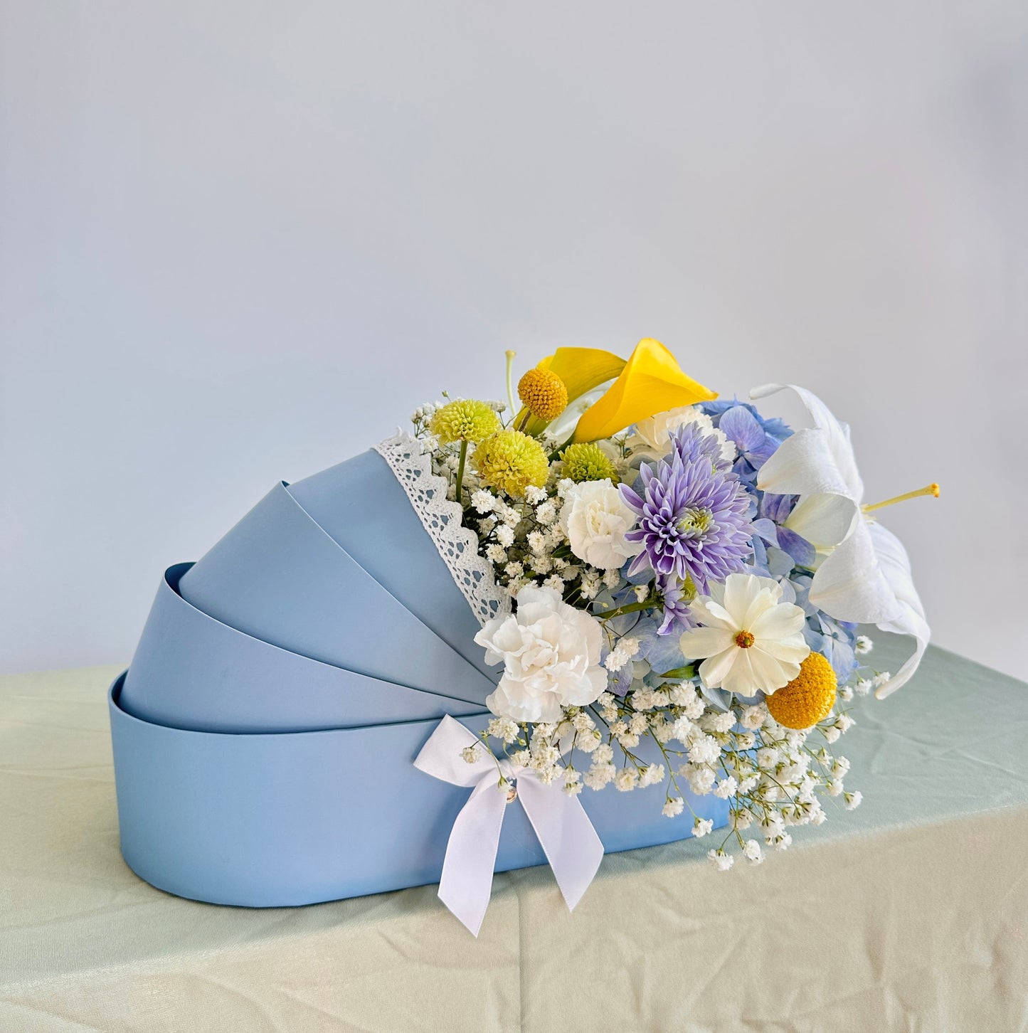 Blue, white, yellow fresh flowers in a blue baby cradle made of recyclable thick paper