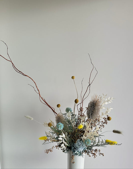 Bouquet of dried flowers held in a white vase against a plain background