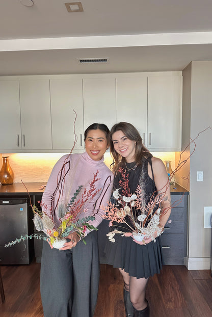 Two women holding floral arrangements in a modern kitchen.