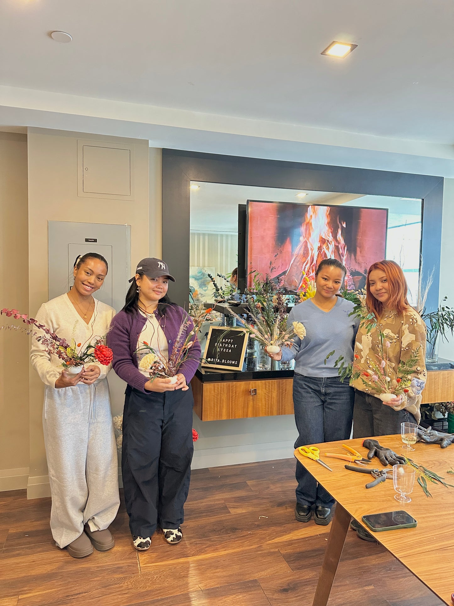 Four people standing in a room with a table and dried ikebana arrangements.