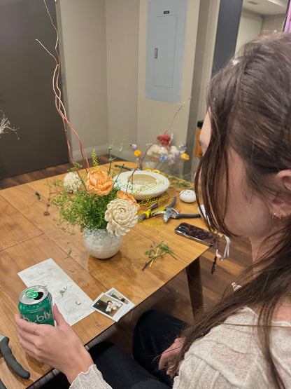 Person sitting at a table with a can of soda and flowers in a casual setting.