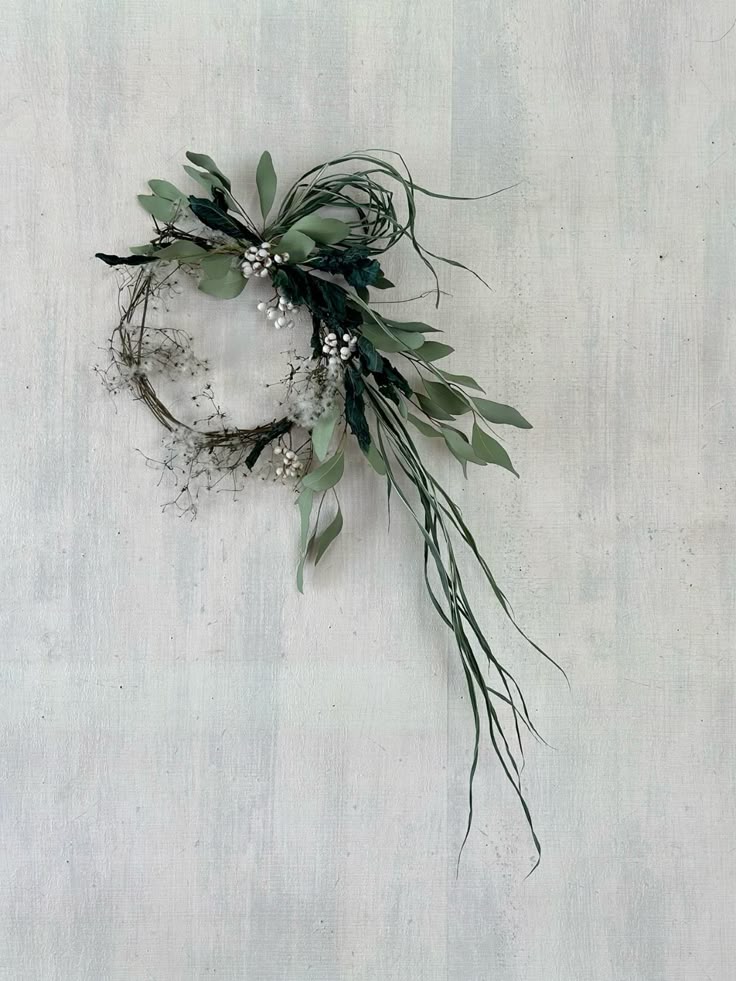 Green leafy wreath with small white flowers on a light gray background