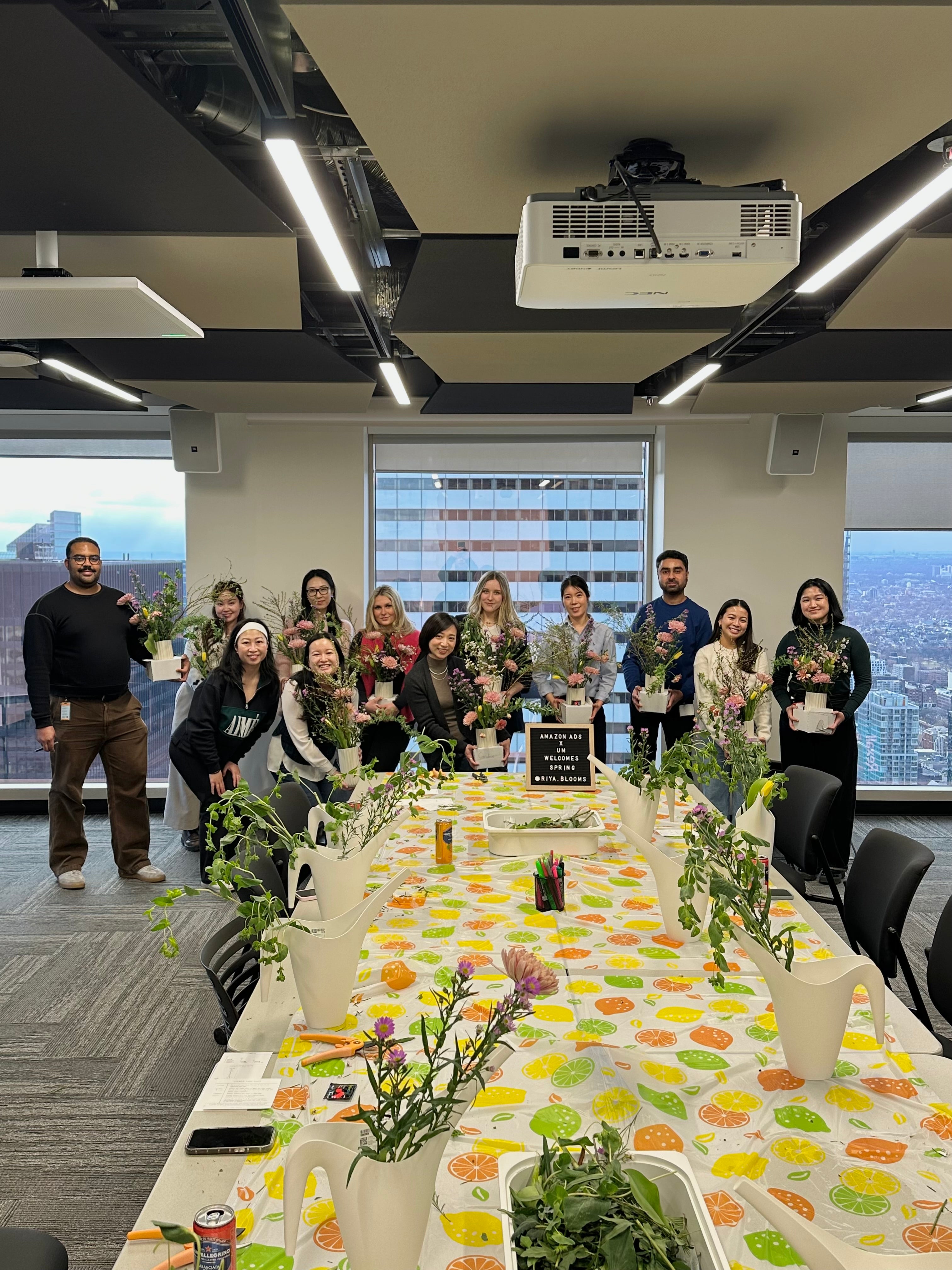 Group of people posing for a photo in an office with flowers and a long table set.