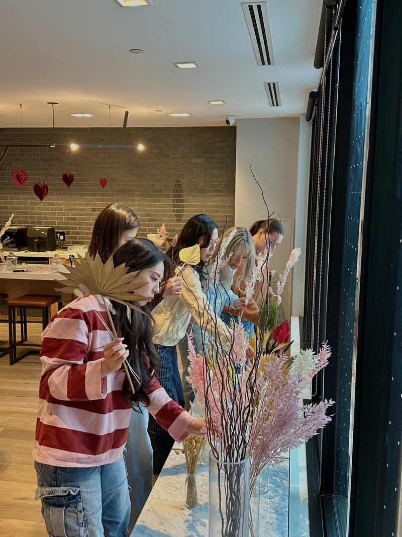 Group of people arranging flowers in a room with a decorative wall.