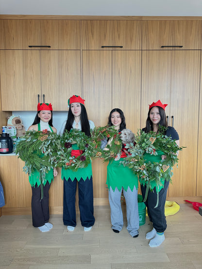 Four people in festive outfits with wreaths and red hats in a kitchen.