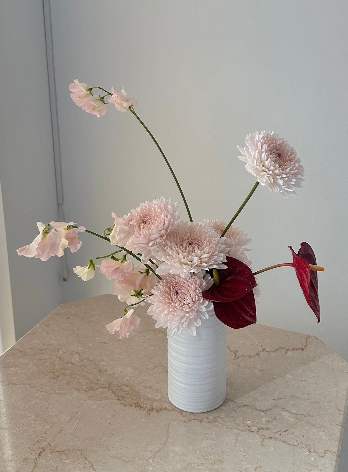White vase with pink flowers on a marble surface