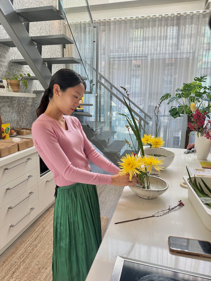 Woman arranging flowers in a kitchen with a staircase and modern decor.
