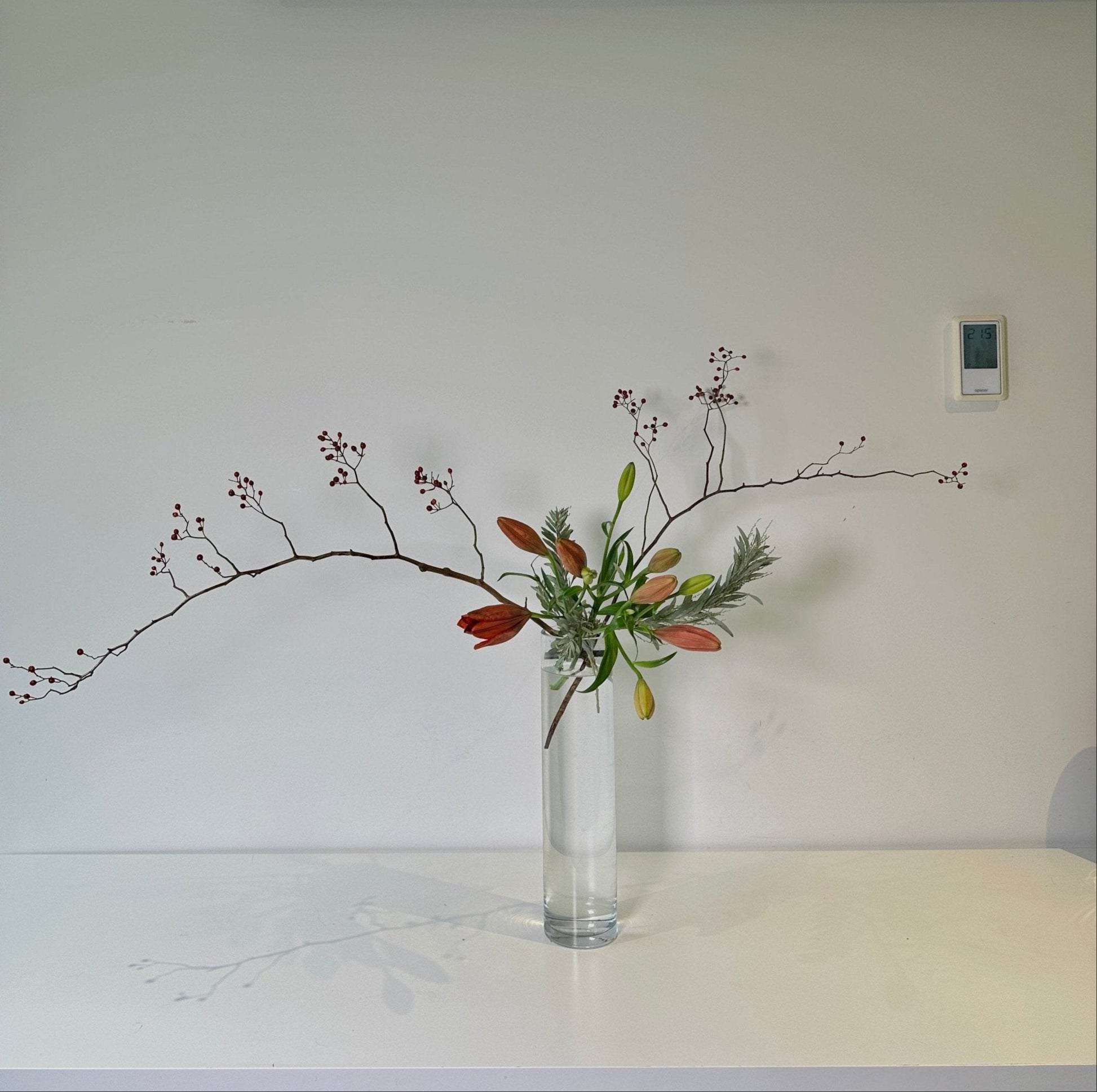 Clear vase with flowers on a white surface against a plain wall