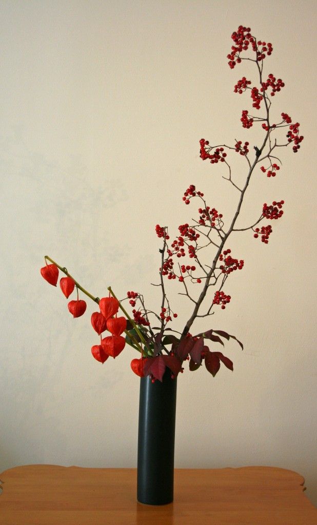 Black vase with red berries on branches against a plain background