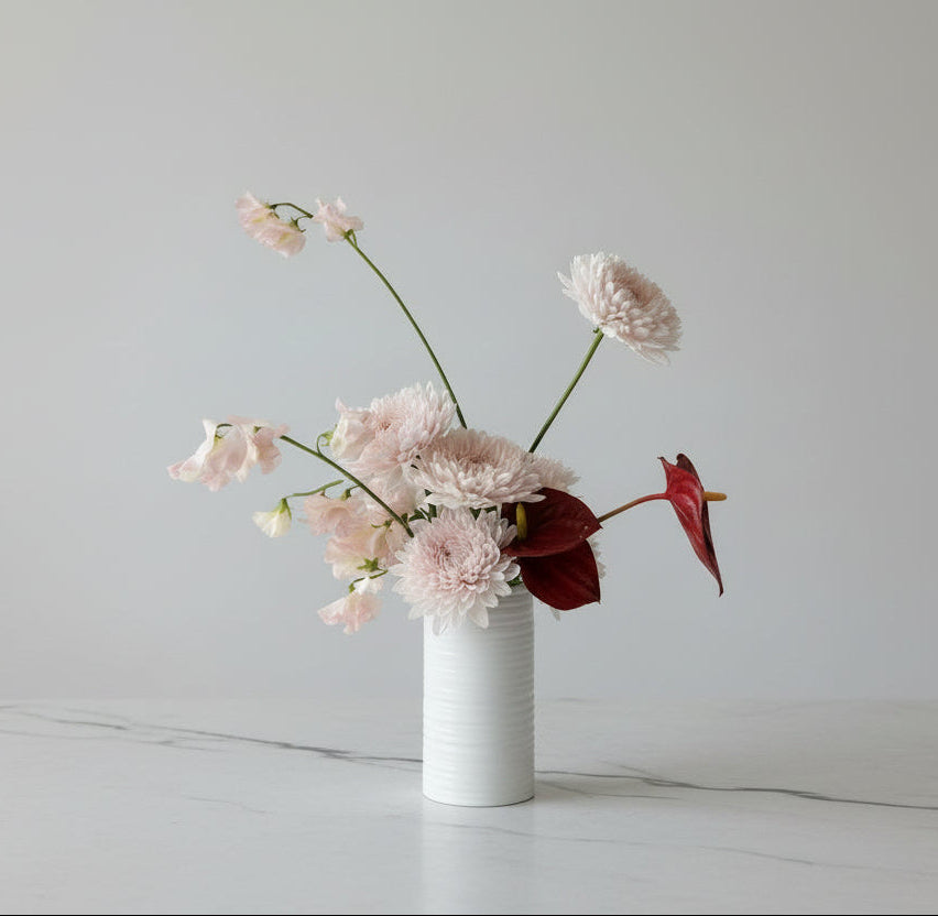 Small white vase with pink flowers on a marble surface