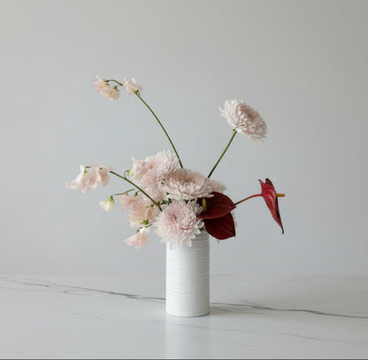 Small white vase with pink flowers on a marble surface