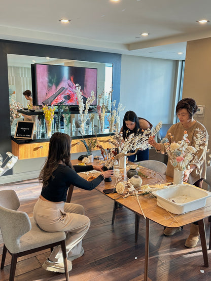 Three women arranging flowers in a modern living room with a television in the background.