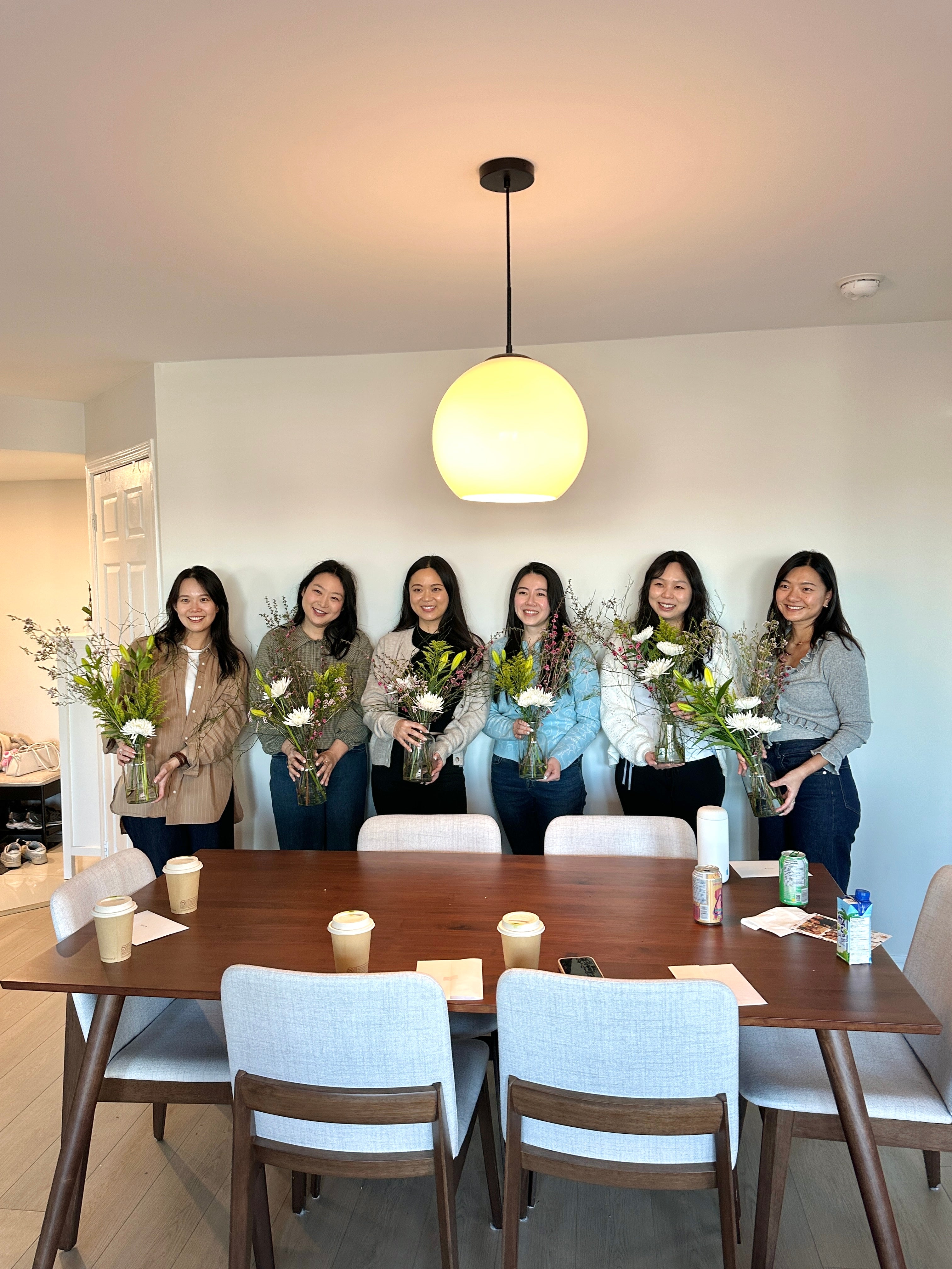 Group of women standing behind a table with flowers and drinks in a modern interior setting.