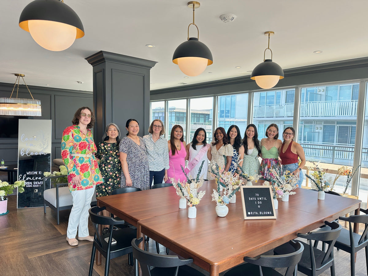 A group of ten women posing together in a modern, bright meeting room with large windows, a wooden conference table, and black pendant lights.