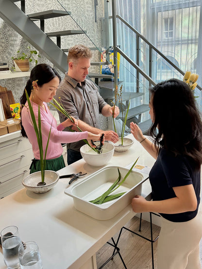 Three people working together on ikebana arrangements in a modern indoor setting.