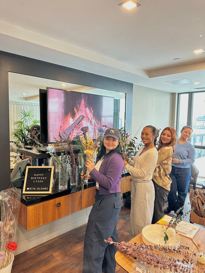 Group of people celebrating a birthday in a modern living room with flowers.