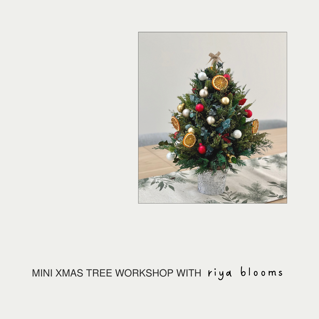 Decorated mini Christmas tree on a table with 'riya blooms' branding.