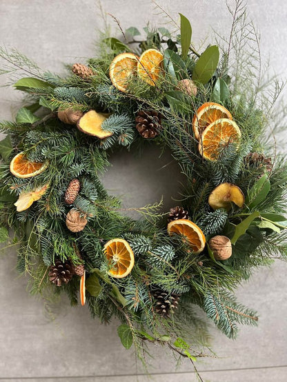 Christmas wreath with greenery, dried oranges, and pinecones on a light background
