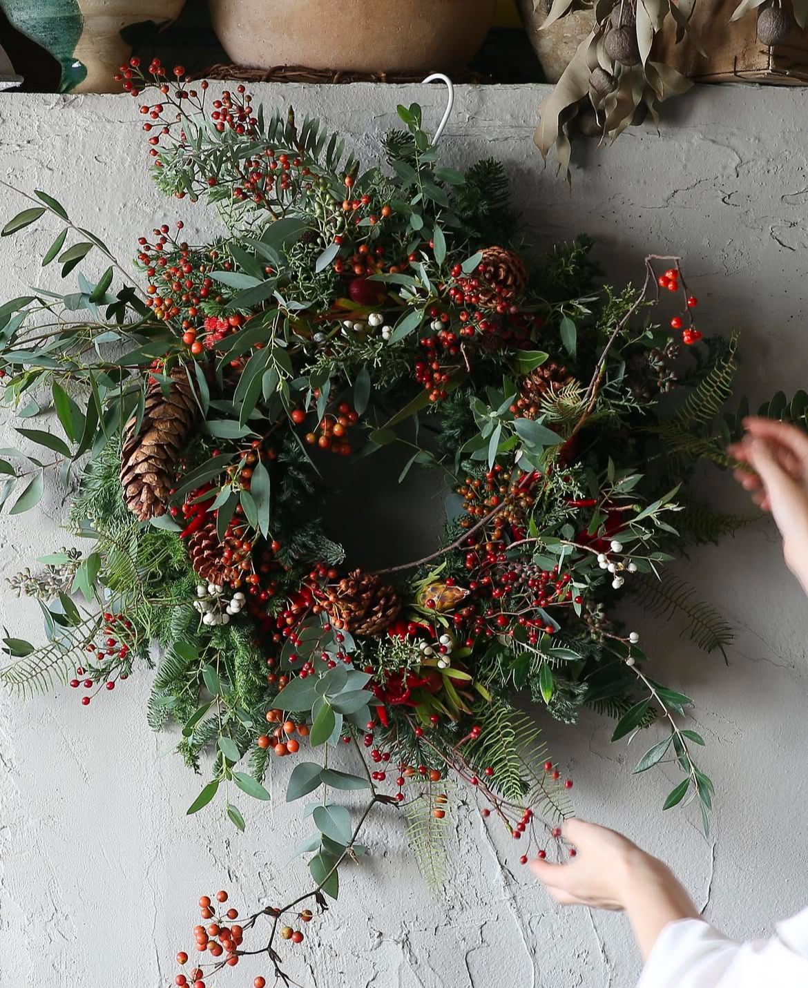 Handmade wreath with greenery and berries on a textured surface