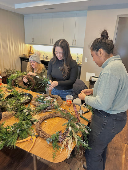Three women making wreaths at a table in a modern room.